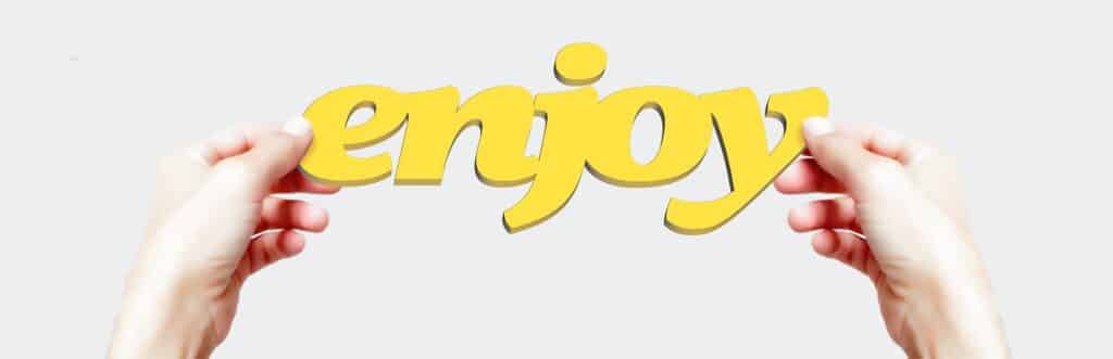 Hands holding up a sign that reads "enjoy" in yellow