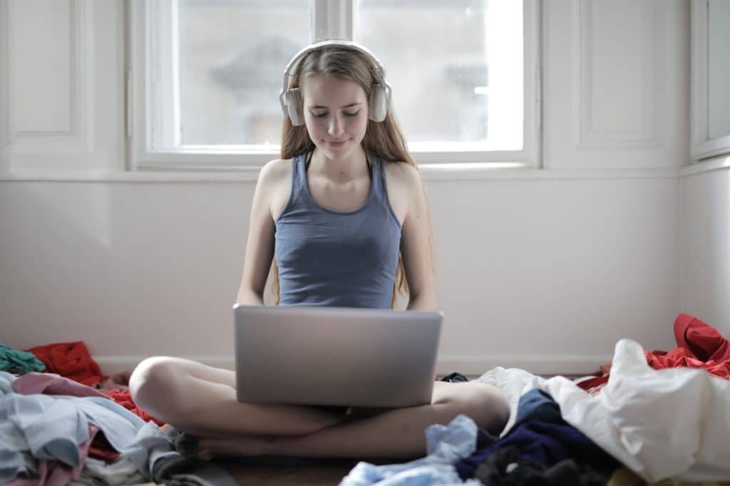 Girl with long blonde hair wearing headphones while typing on laptop.