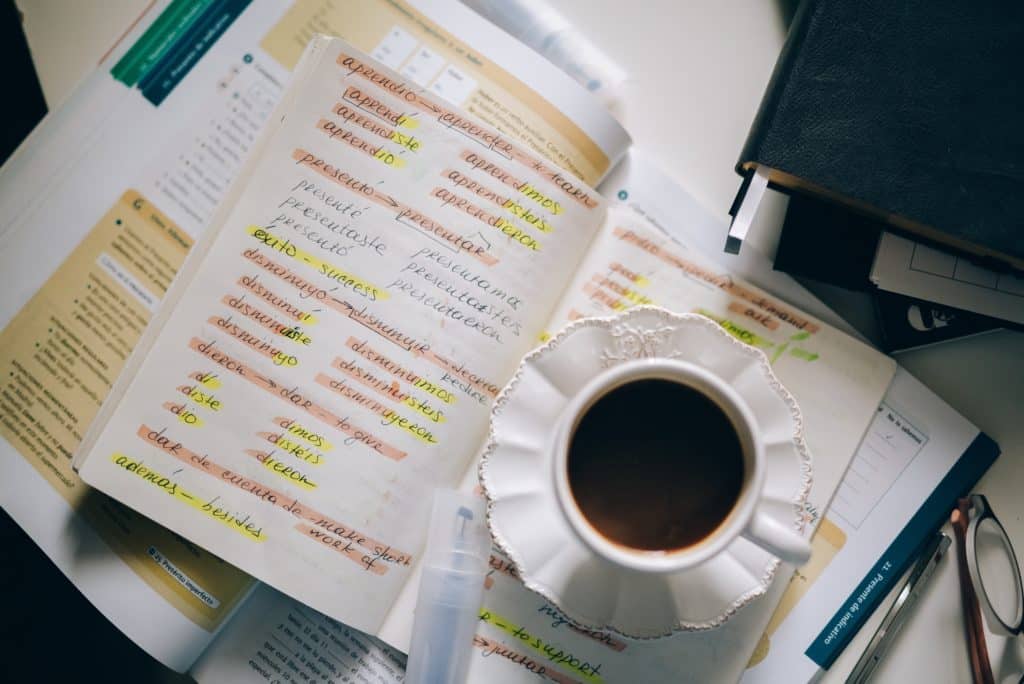 A cup of tea sitting atop books with words written in Spanish and highlighted.