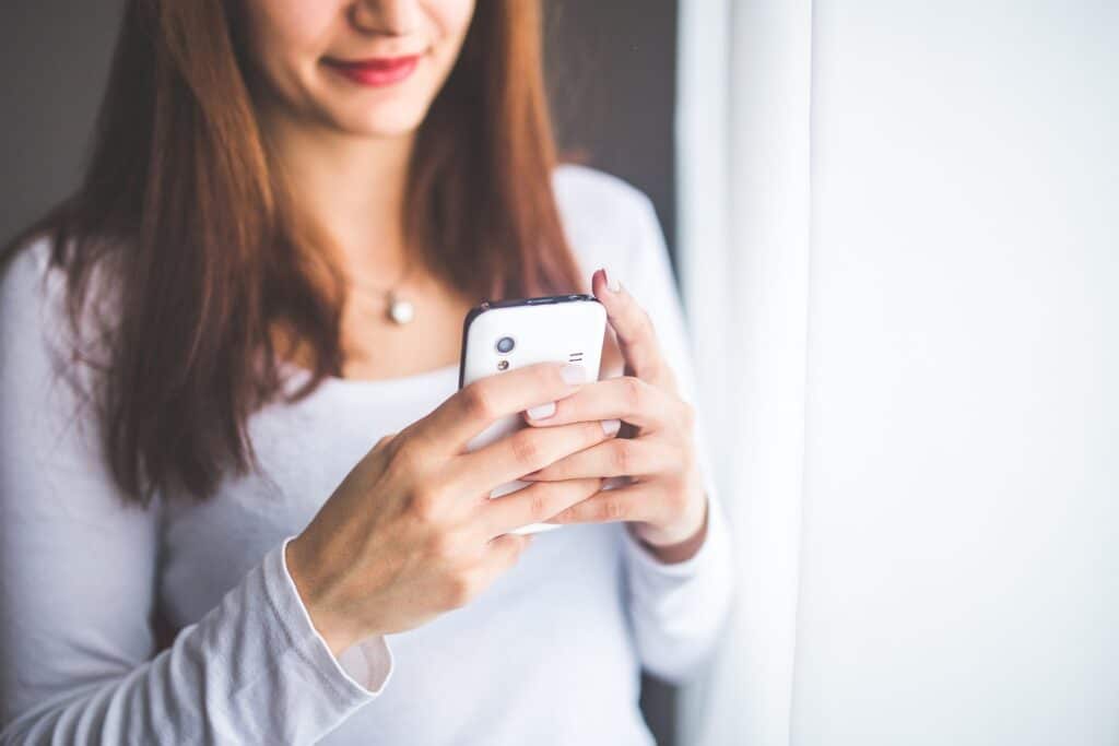 Woman in a white shirt holding a white smartphone.