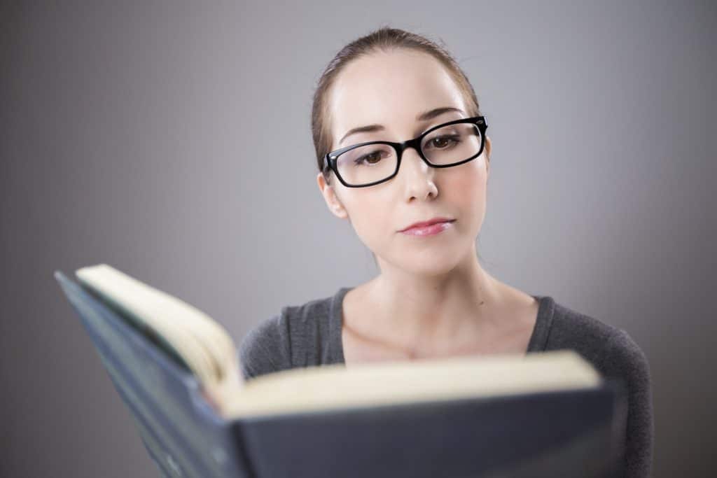 Woman in grey wearing glasses and reading a book