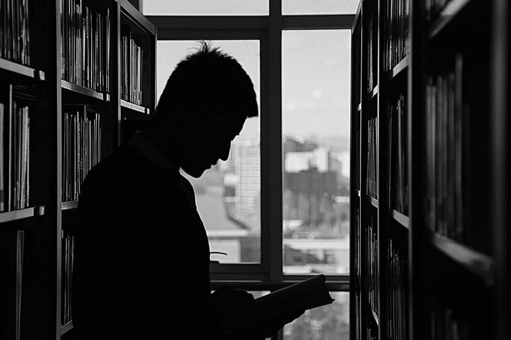 Silhouette of a man reading a book in a library.