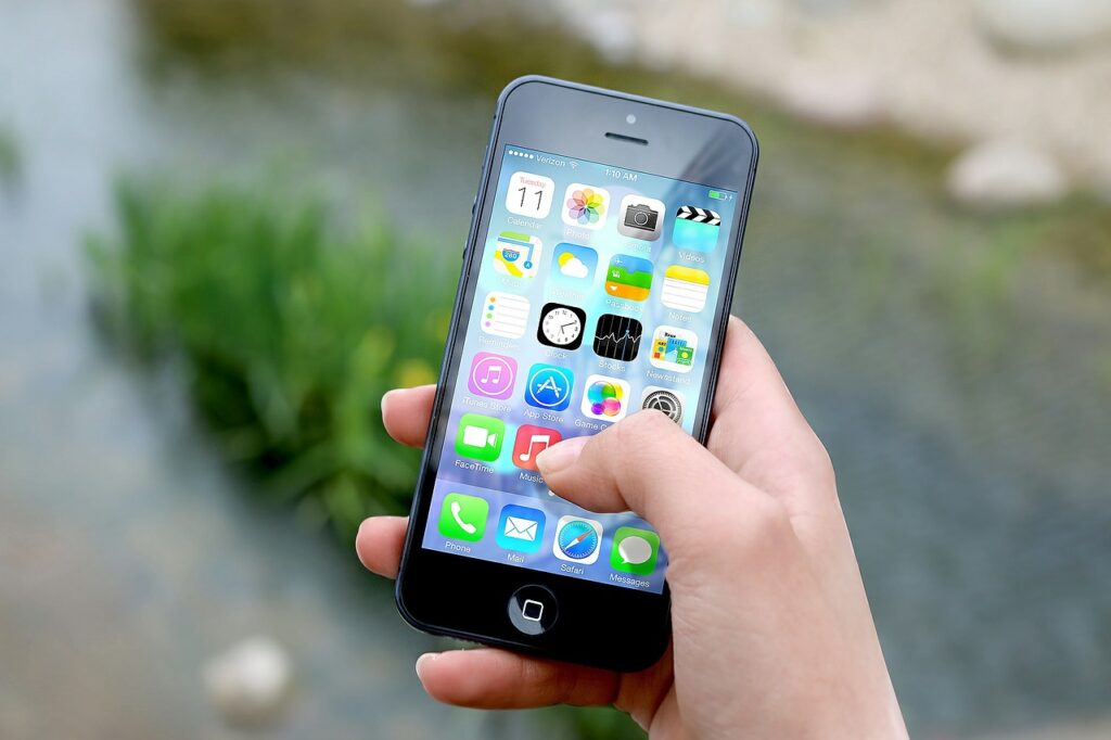 Close-up of a hand holding an iPhone displaying numerous apps