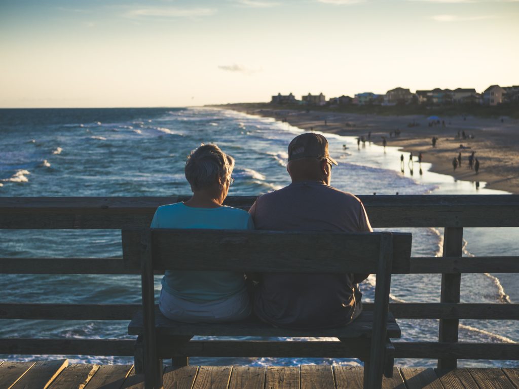 A retired couple sitting on a bench looking at water.