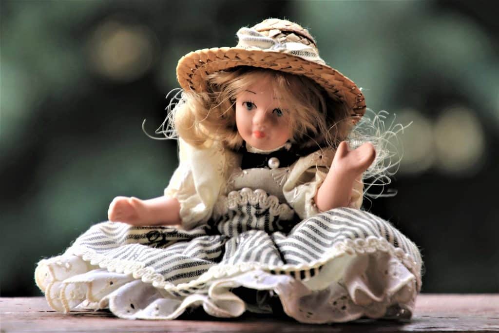 Small porcelain baby doll with long blonde hair wearing a straw hat and black and white dress.