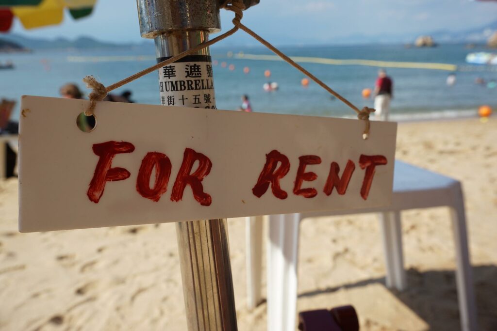 A sign that says "For Rent" in red on a beach umbrella.