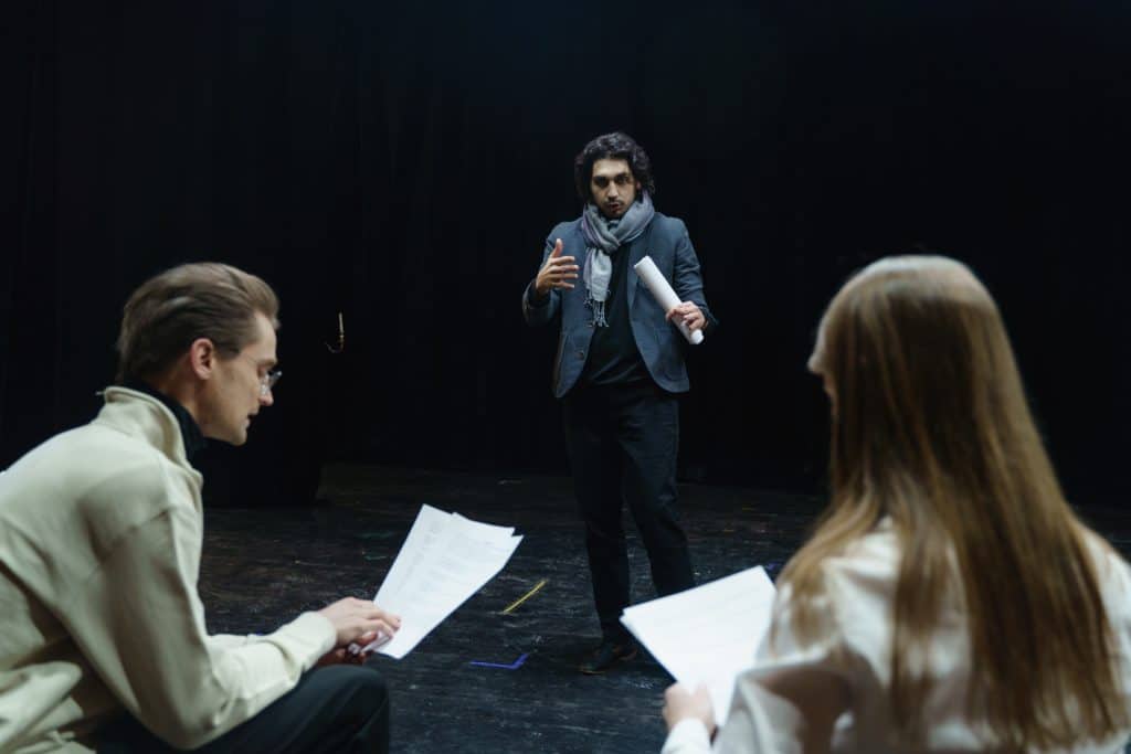 A man in a scarf auditioning in front of a seated man and woman