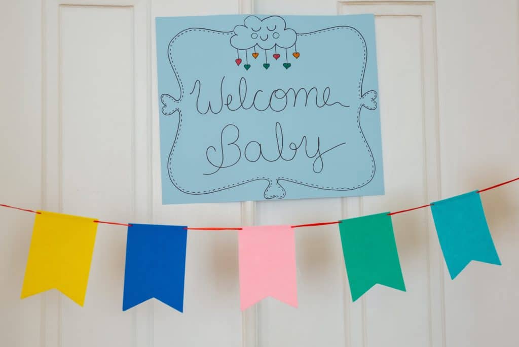 A blue sign that reads "Welcome Baby" over a multi-colored flag banner.
