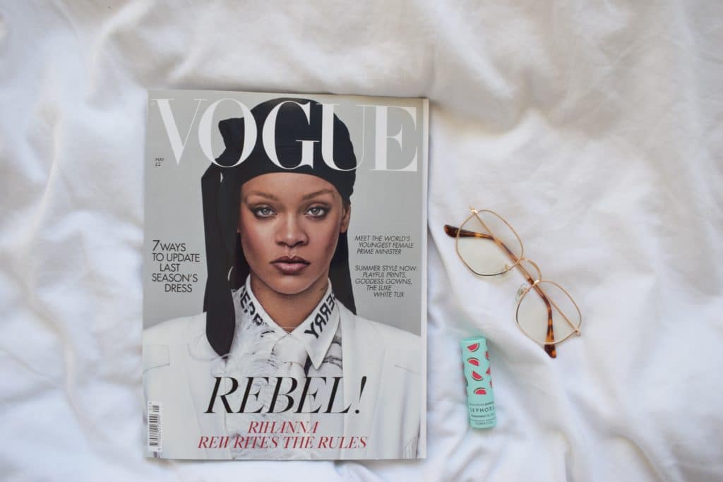 Glasses, lipstick, and an issue of VOGUE magazine with Rihanna on the cover sitting atop a white sheet