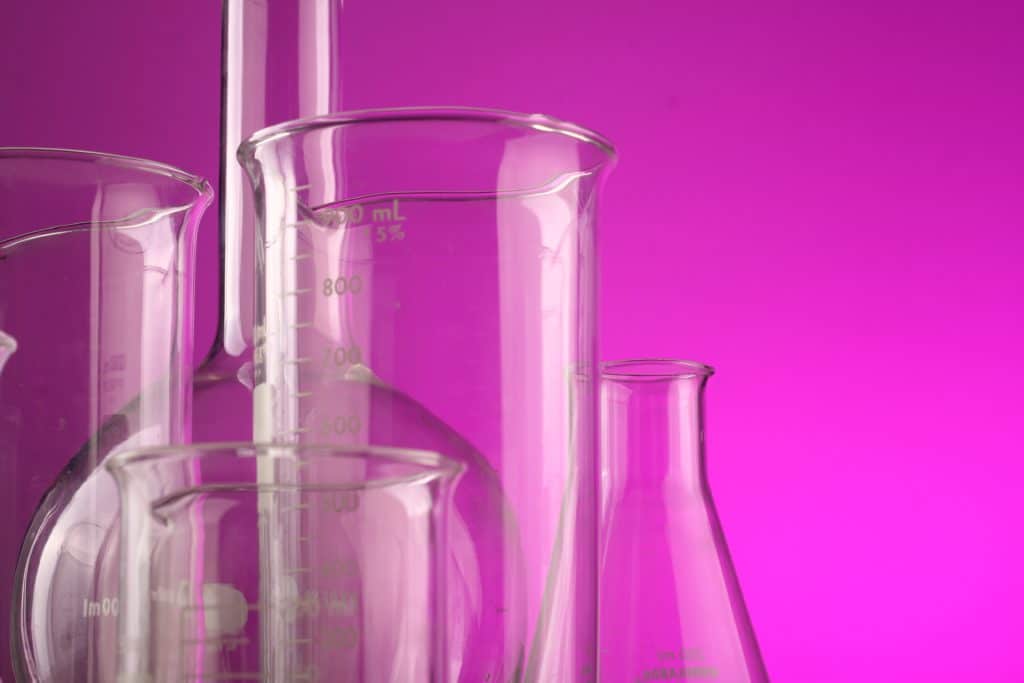 Clear glass beakers and measuring cups against a magenta background