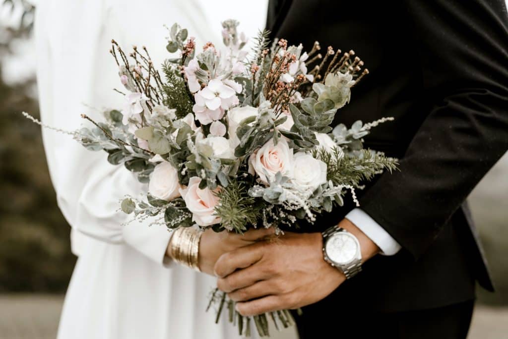 Closeup of a bride and groom's hands holding a wedding bouquet