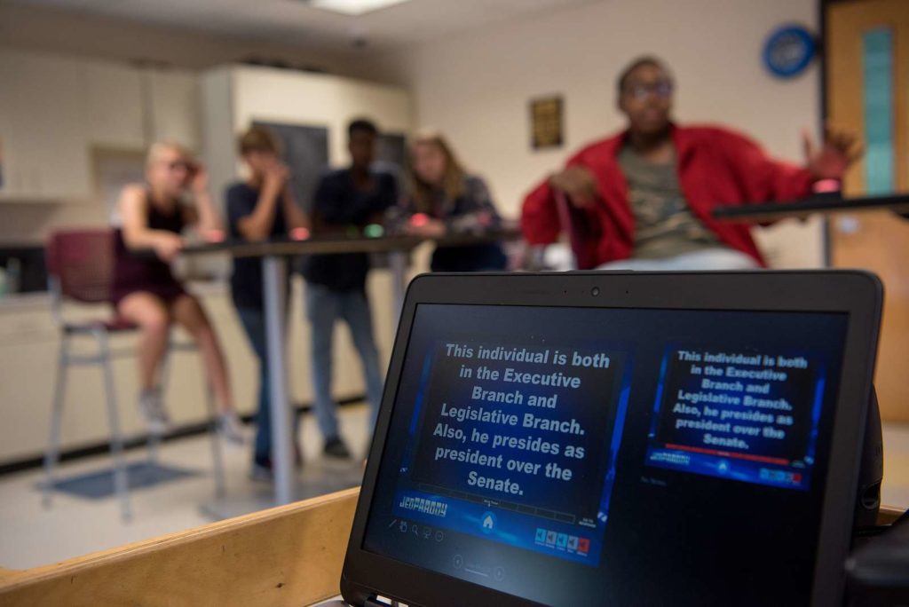 A screen displaying Jeopardy! clues in front of teens at school