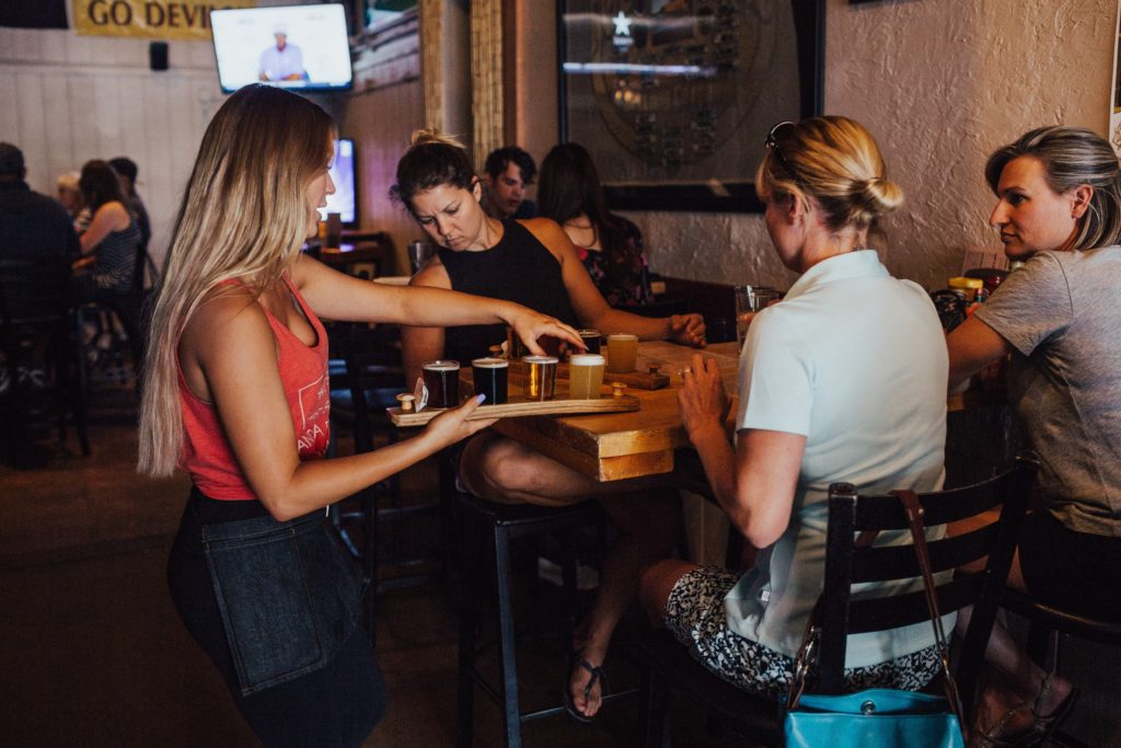 Female bartender serving beers to a group of girls at a table