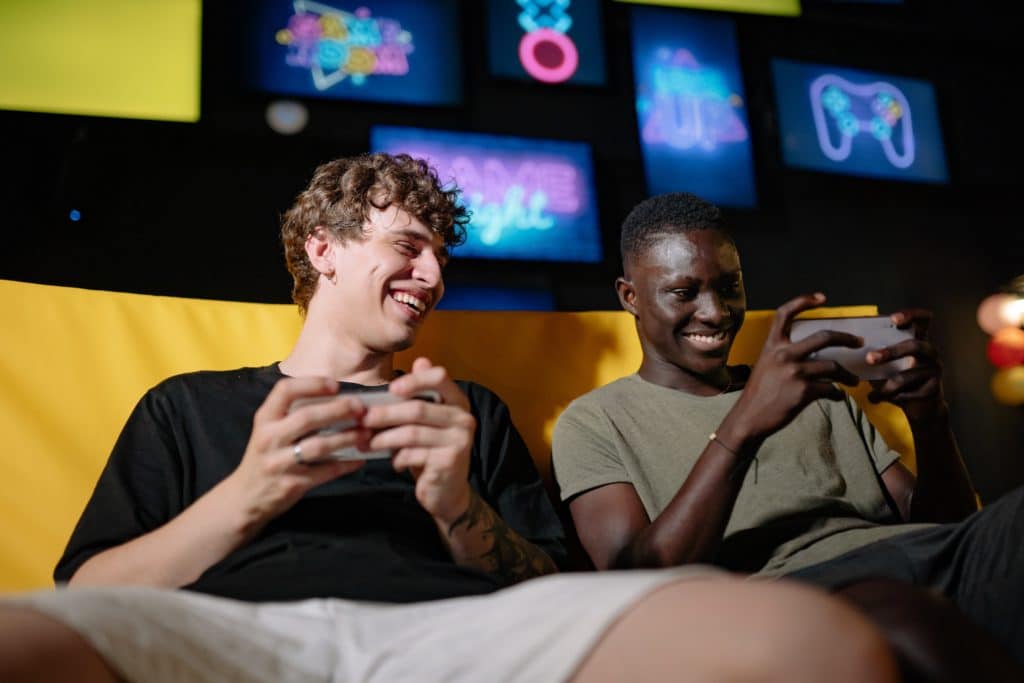 Two young men sitting on a yellow couch playing on their smartphones