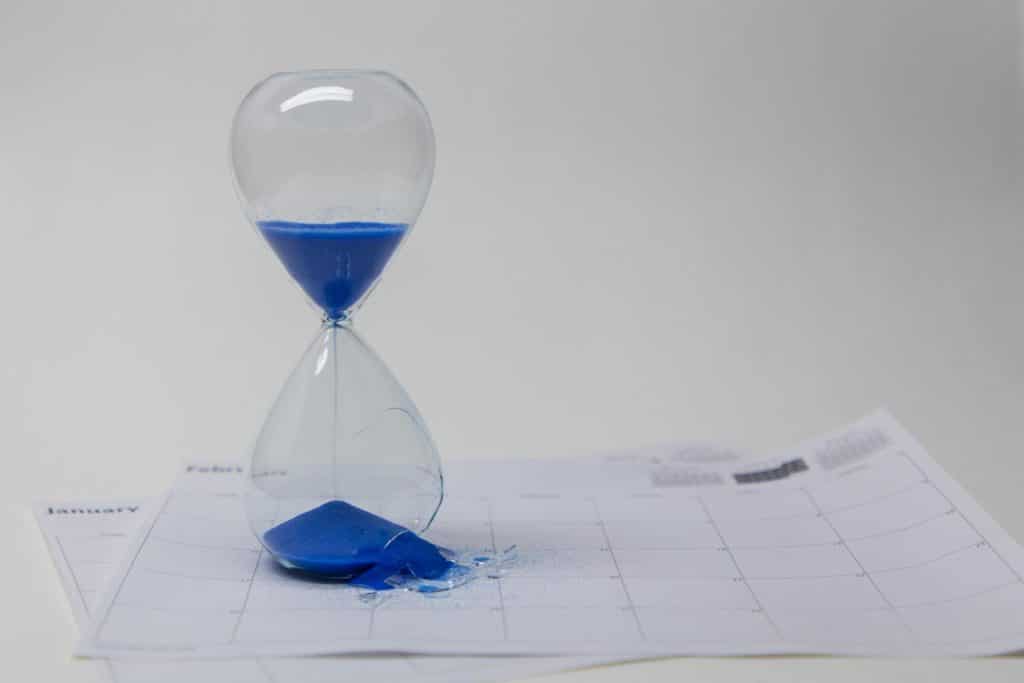 Blue sand in an hourglass on top of calendar sheets. 