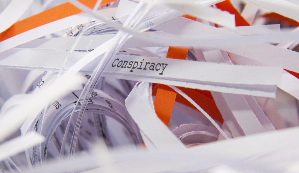A bunch of shredded up white and orange papers with one that reads "conspiracy"