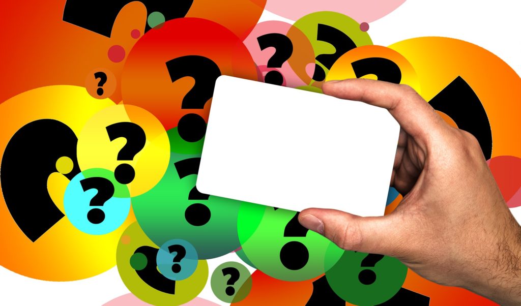 A hand holding up a blank white card with multicolor question marks behind it