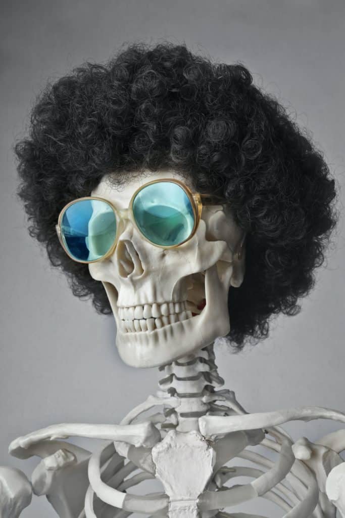 A skeleton wearing a curly wig and sunglesses