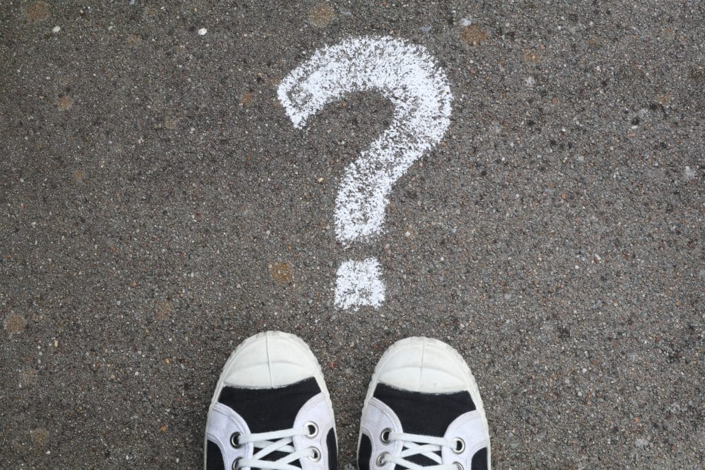 A question mark written in chalk on concrete with a pair of sneakers in front of it
