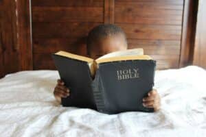 Photo of a small child reading the Bible in bed.