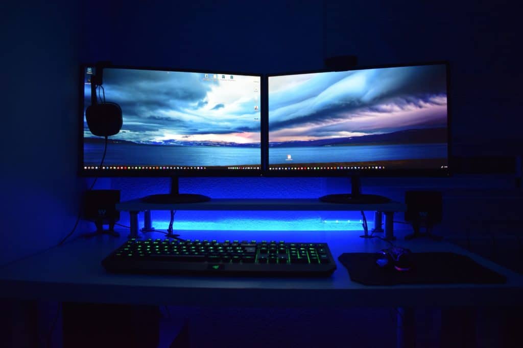 Two desktop monitors next to each other with a keyboard and headphones, displaying a sky wallpaper