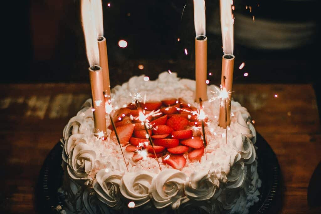 A vanilla cake with strawberries in the middle, and candles and sparklers on top.