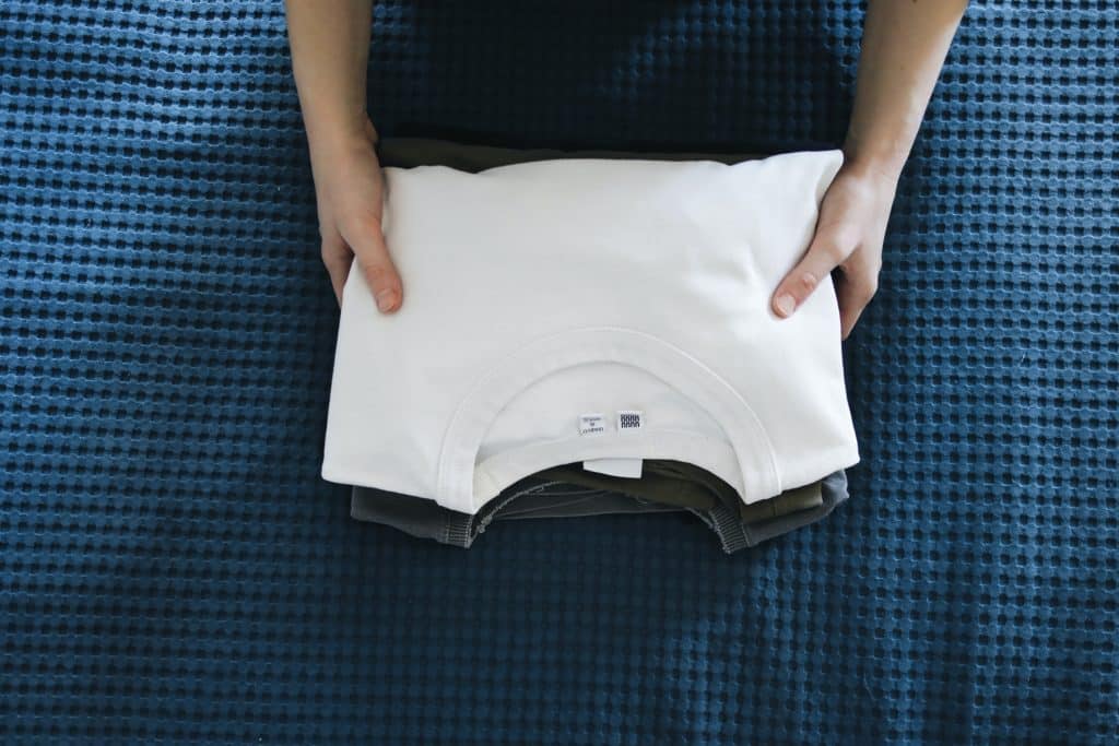A person holding a pile of neatly-folded t-shirts.