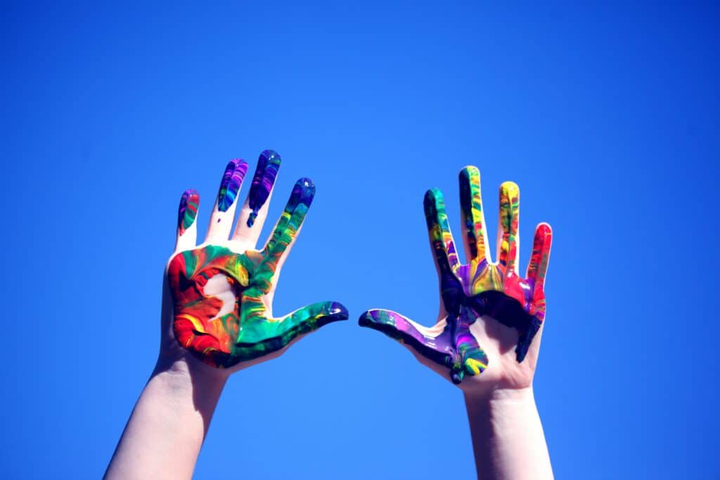 Photo of a person's hands covered in paint against a blue background.