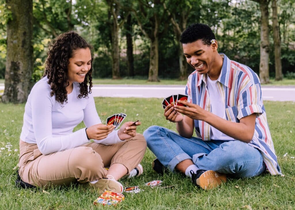 Image of a man and a woman sitting on the grass in a park playing a game of Uno.