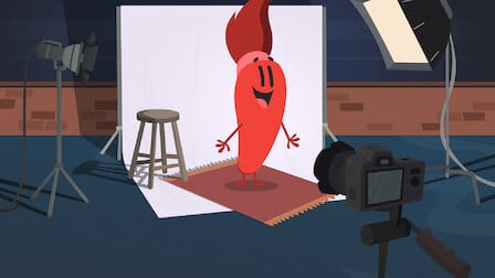 Tina, the red paintbrush character, from Netflix's Trivia Quest. Tina is standing in front of a stool and a white background with cameras filming her. 