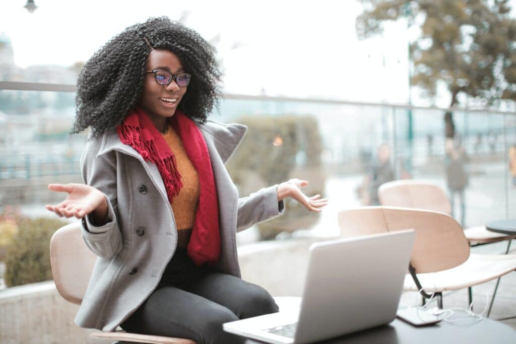 A young woman sitting outside wearing glasses and a scarf and video-chatting on her laptop