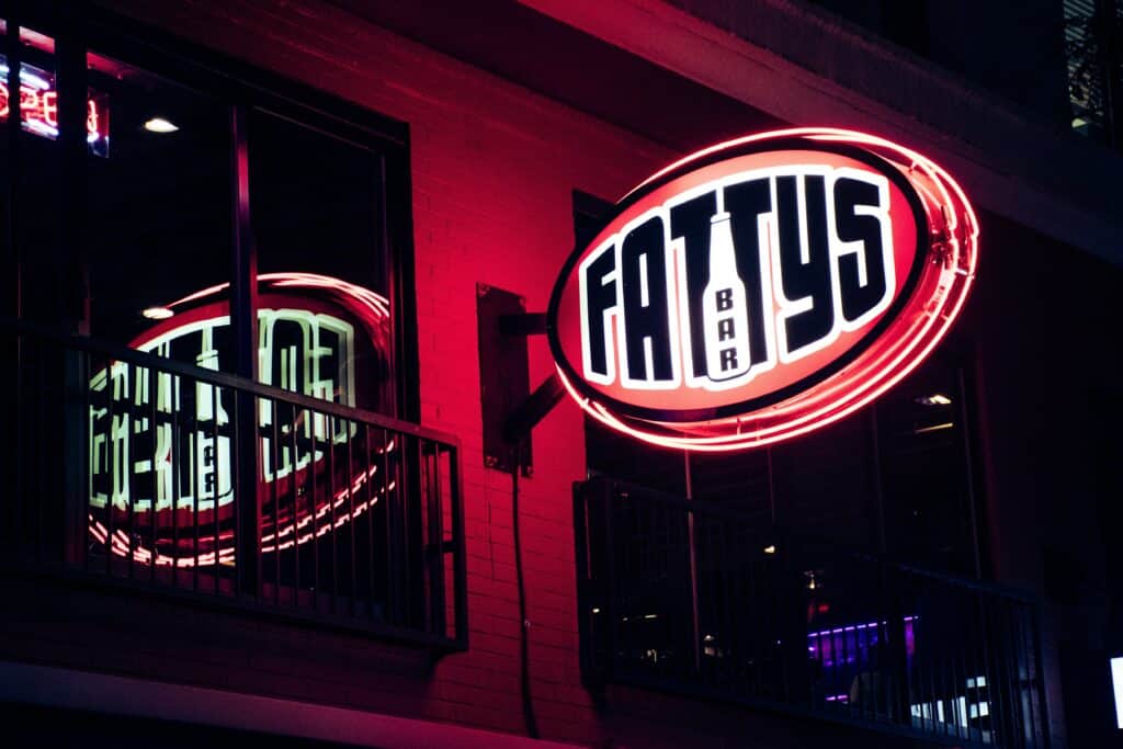A lighted sign at night that reads "Fattys Bar"