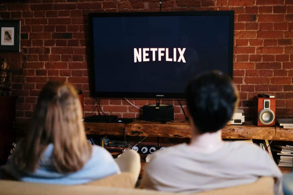 Two people sitting on a couch watching Netflix on a TV screen