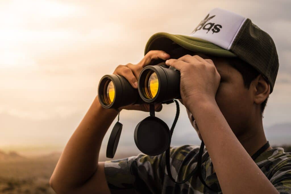 Man in an Adidas hat looking through a pair of binoculars