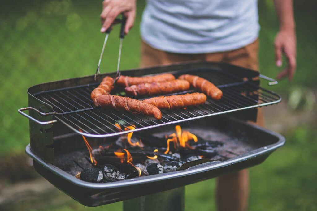 A man cooking on a grill with hot dogs on it