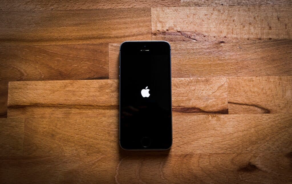 Black iPhone displaying the apple start screen on top of a wooden background