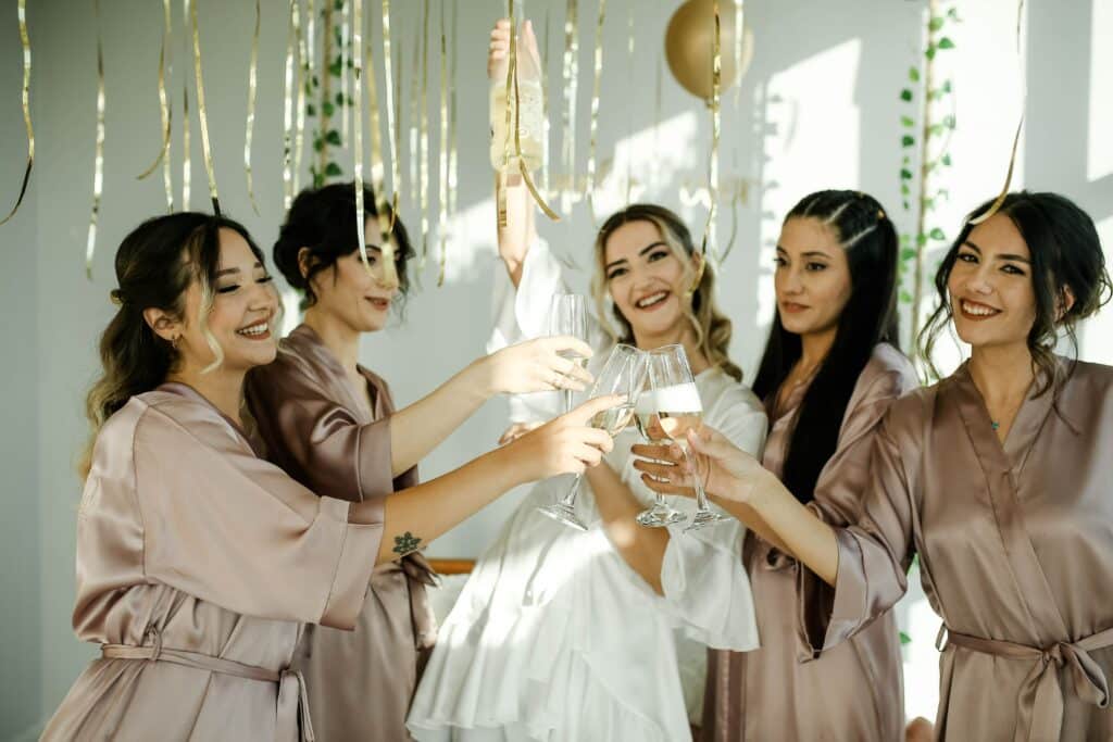 A bride and her bridesmaid in matching robes clinking glasses of champagne