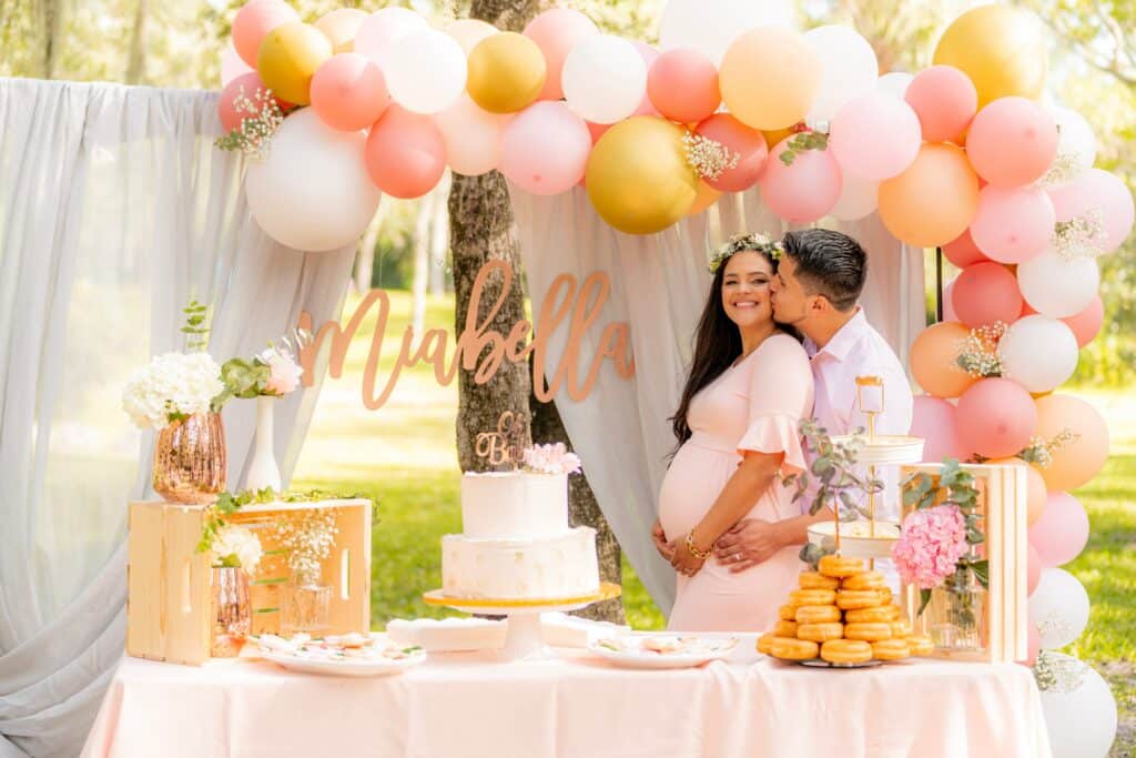 A man and pregnant woman standing next to a cake at a baby shower