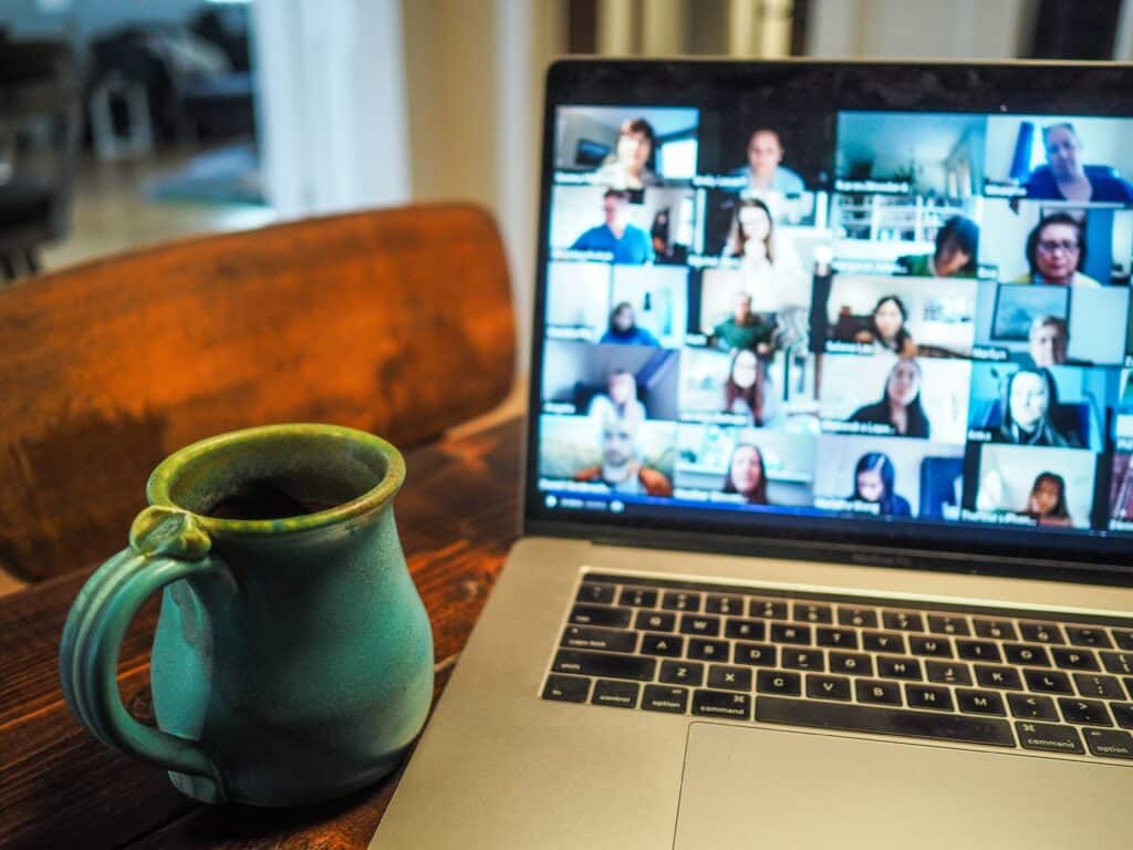 Photo of an open laptop displaying a Zoom screen with multiple people joined, next to a mug of coffee