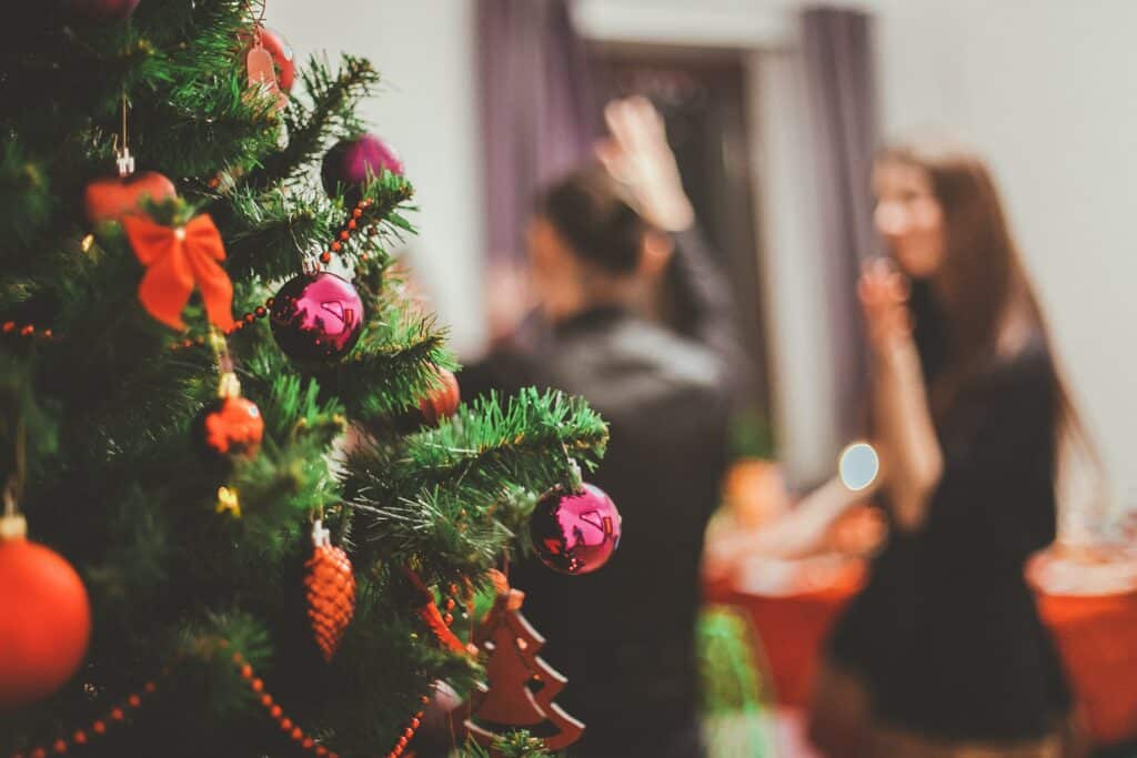 Photo of a Christmas tree in focus, with people attending a party out of focus in the background