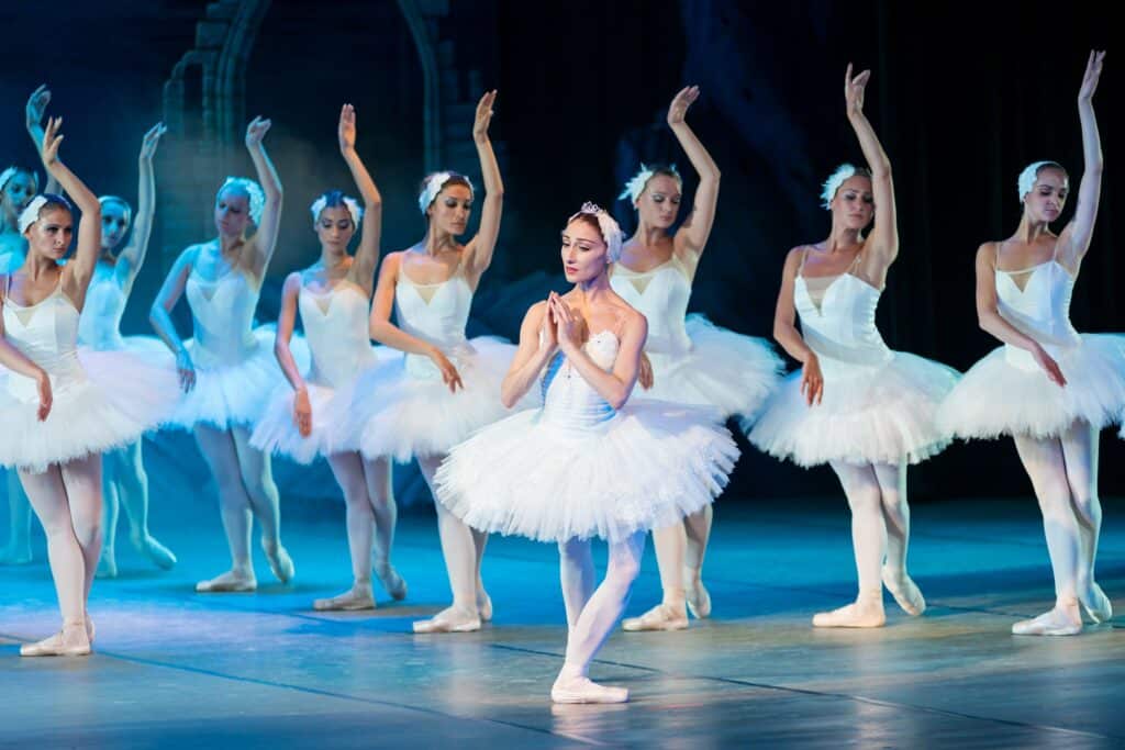 Numerous female ballet dancers performing in matching white tutus