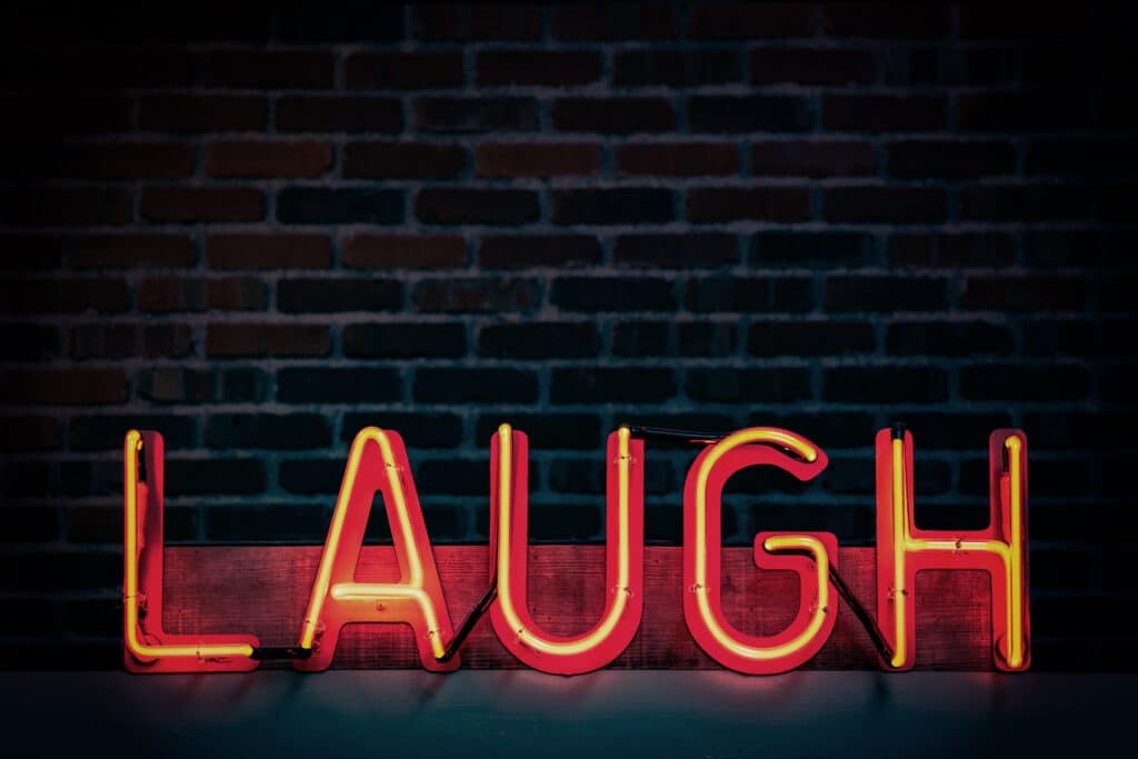 A neon sign that reads "LAUGH" in front of a brick wall