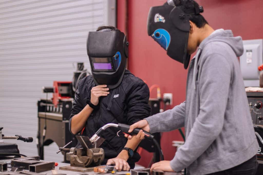 Photo of two students in shop class wearing welding masks.