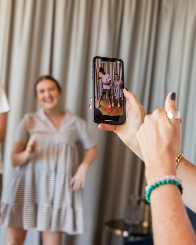 Photo of two people dancing while being recorded on a smartphone.