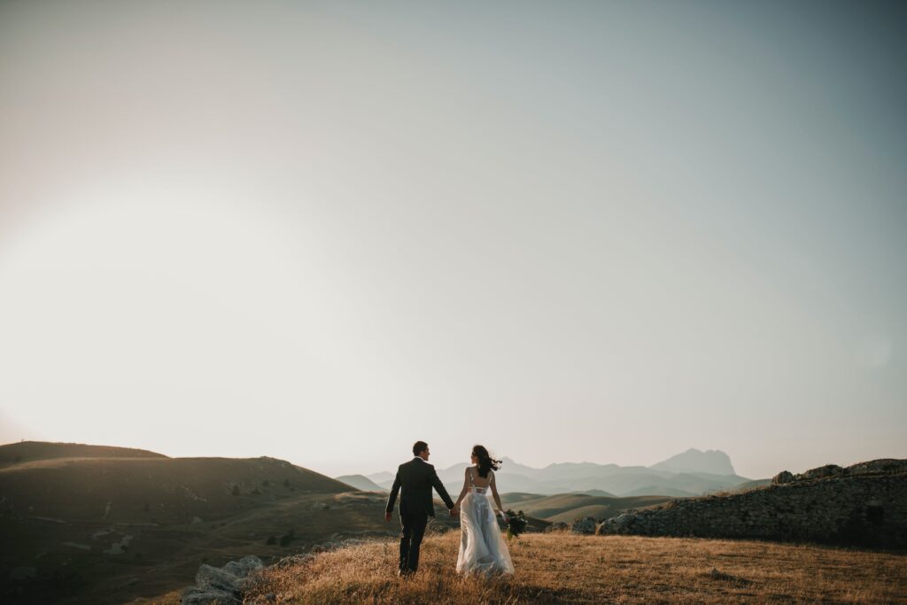 Photo of a bride and groom holding hands and walking into the mountains