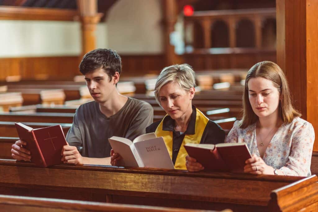 A man and two women sitting in a pew at church, reading Bibles