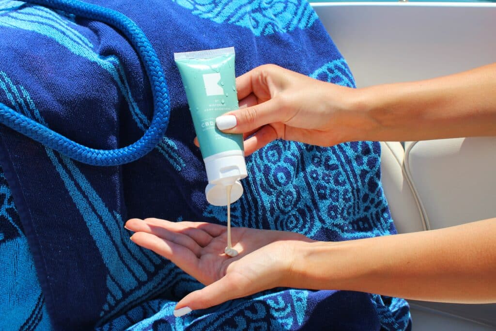 Photo of a woman squeezing sunscreen onto her hand in front of a beach towel