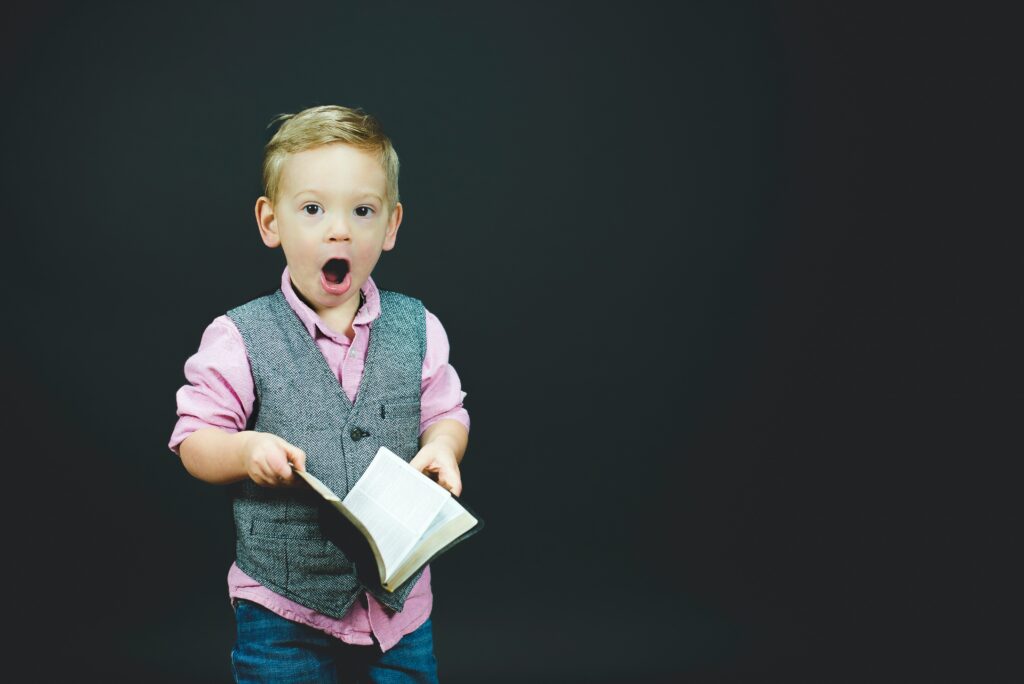Photo of a small blonde boy holding open a book and looking surprised