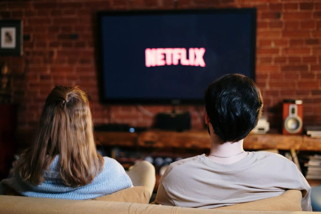 Behind shot of a couple watching TV with the Netflix logo blurred in the background