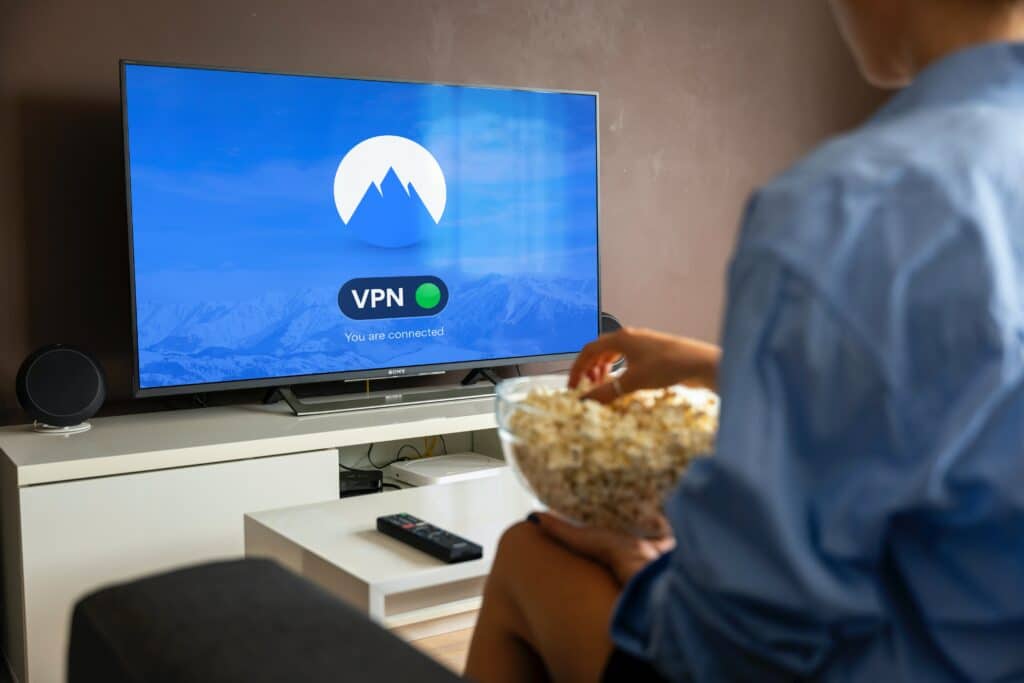Person on a couch eating popcorn, watching a TV displaying a blue VPN screen.